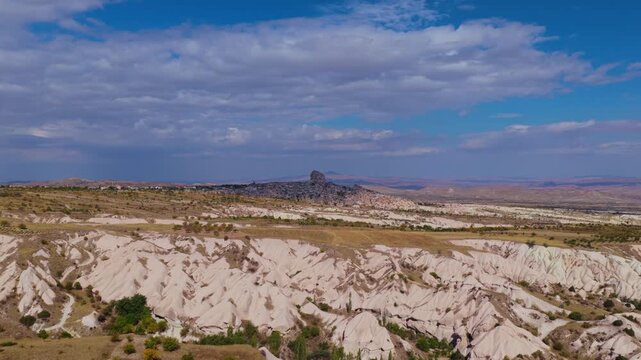 Aerial wide view of Uchisar Castle rising above Cappadocia landscape in Turkey, surrounded by unique rock formations and valleys under a dramatic cloudy sky