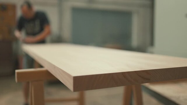 Carpenter sanding a wooden tabletop in a workshop