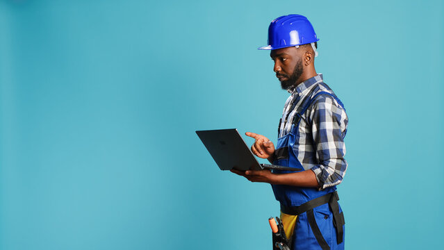 Modern constructor using laptop to find inspiration for building project, browsing online and making calculations or measurements on camera. Construction worker holding wireless pc to work.