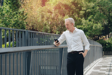 Fototapeta premium Middle aged man smartphone outdoor casual white shirt black pants railing trees sunlight urban setting