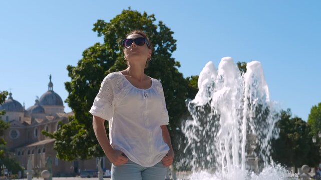 Tourist enjoying summer sun near fountain in Italy. Young woman wearing sunglasses and casual clothes is posing near fountain in prato della valle square, padua, italy, enjoying summer sun
