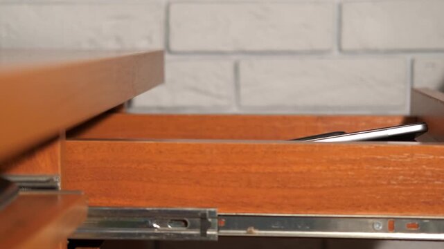 Hand hiding smartphone and tablet in a secret drawer. Clandestine action of opening a secret drawer a smartphone and a tablet, representing concepts like privacy, addiction, parental control