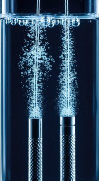 Close-up of metal electrodes in a clear electrolysis cell generating streams of hydrogen and oxygen gas bubbles for green energy research, sustainability, fuel, reaction