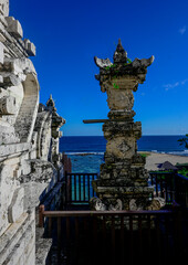 Obraz premium Captivating Bali coastal scene featuring weathered traditional temple stone carvings and a pillar. Framed against a deep blue sky, a pristine turquoise ocean, and a sandy beach. Perfect for travel, we