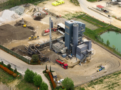 Aerial view of an industrial asphalt plant with heavy machinery, gravel piles, and a large processing tower in San Giovanni Valdarno, Tuscany, Italy.