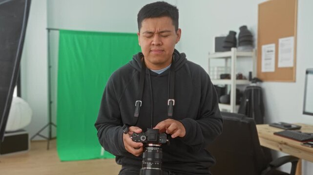 Man adjusting a camera with hands in a studio with green screen and softbox, checking settings and rubbing his eye between shots; quiet concentration.