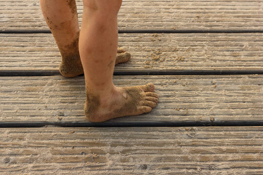 Bare feet of child covered with sand on wooden pier in summer