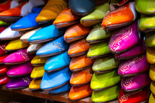 A vibrant display of colorful traditional Moroccan leather babouche slippers stacked closely on a wooden shelf in a market stall in the medina of Marrakech Morocco showcasing traditional craftsmanship
