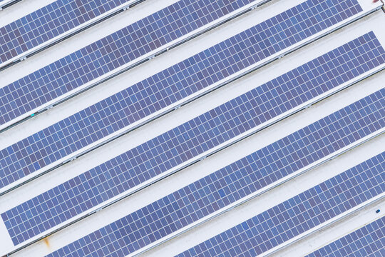 Aerial view of solar panels arranged in diagonal rows on a white industrial roof in Leccio, Toscana, Italy.