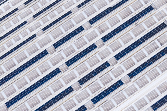 Aerial view of photovoltaic solar panels arranged in diagonal rows on a large industrial roof in Leccio, Toscana, Italy.