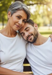 Obraz premium Mature woman and young man sitting on park bench. Mother with son hugging together. Family relationship, support and unconditional love. Emotional bond between parent and adult child.