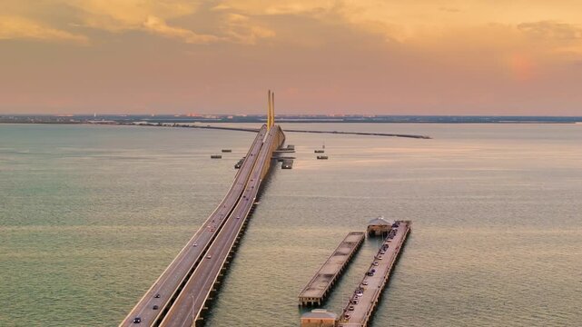 Fishing pier and highway road at sunset. Driving traffic cars on Sunshine Skyway Bridge over Tampa Bay in Florida. Transportation infrastructure in USA