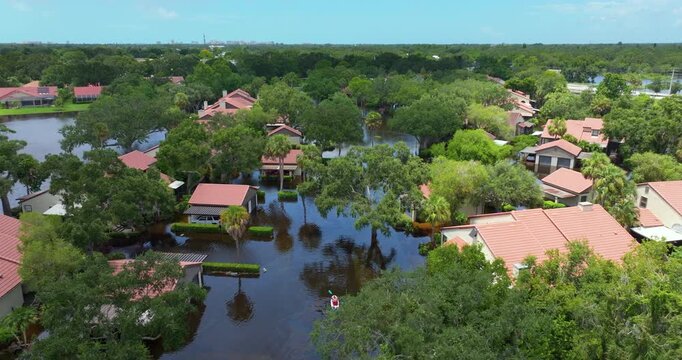 Flooding victims kayaking on suburban street in Florida. Rainfall flood waters between rural homes in residential area.