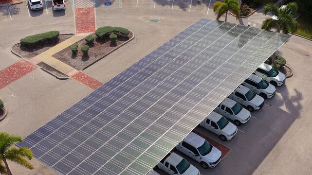 Green electricity generated from solar panels installed as shade roof over parking lot with parked cars. Photovoltaic technology integrated in city infrastructure.