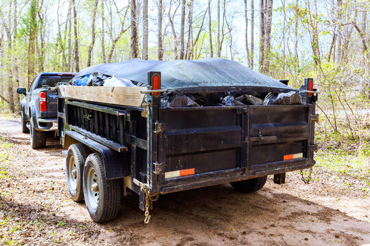 Trailer carries waste materials on dirt road in forested area