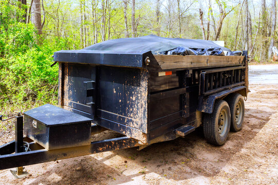 Black trailer parked on dirt road surrounded by trees near wooded area