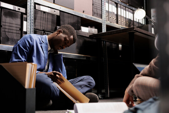 Overworked private investigators discussing case evidence, working late at night at criminology investigation in arhive room. Diverse police officer searching for clues, trying to catch suspect