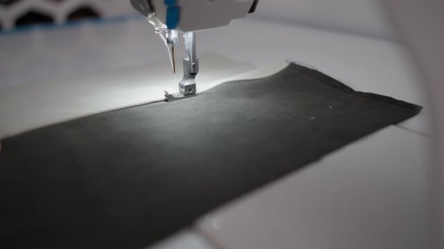 Tailor sewing piece of black fabric with focus on sewing machine in workshop creating clothing piece with precision