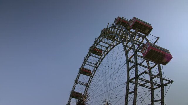 4K low-angle shot of the historic Wiener Riesenrad against a clear twilight sky. The red gondolas of the world's oldest operational ferris wheel rotate in real time, capturing the imperial charm of Au