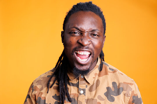 Furious stressed man having breakdown while posing aggresive in studio over yellow background, showing unpleasant reaction. African american young adult feeling frustrated and mad