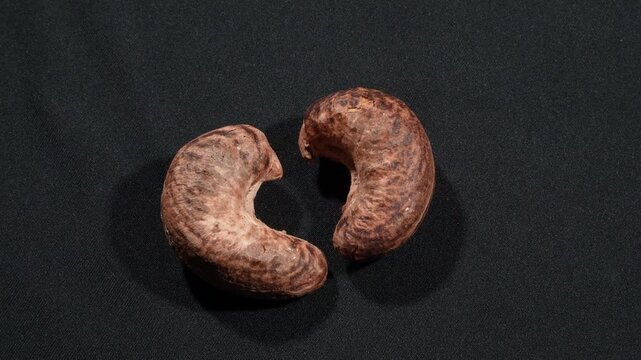 Close-up of two cashews forming a heart shape rotating on black, minimalist.