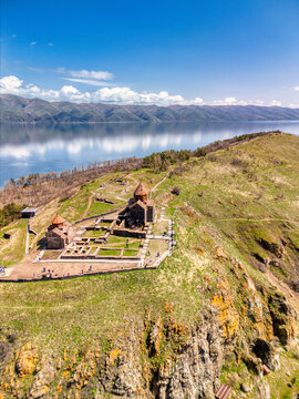 Aerial view of Sevanavank monastery complex with people walking along paths overlooking the calm blue waters of Lake Sevan under a clear sky in Sevan, Gegharkunik Province, Armenia.