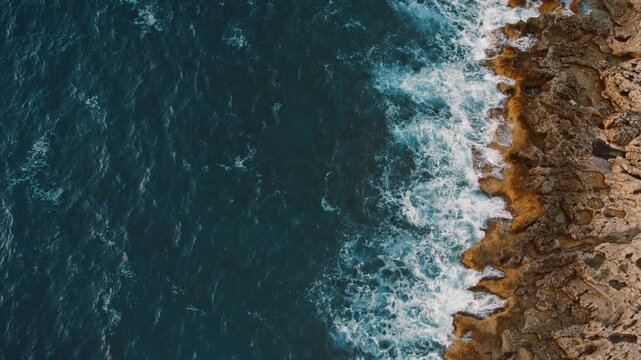 Sea waves crash against eroded rocky shore viewed from above