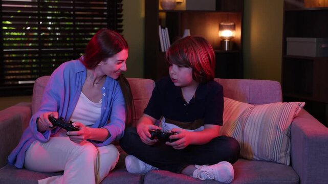 Happy mother and son with controllers playing video game on sofa at home