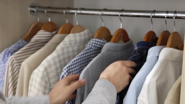 Man putting hanger with shirt into wardrobe indoors, closeup
