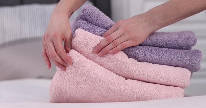 Woman with stack of soft towels on bed indoors, closeup