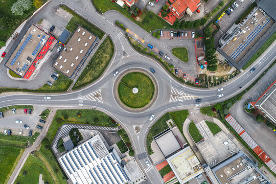 Aerial view of a traffic roundabout with cars surrounded by industrial buildings featuring solar panels and green spaces in Leccio, Toscana, Italy.