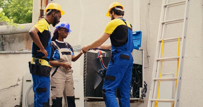 Diverse team of experienced mechanics brainstorming possible ways to recondition defective outdoor condenser. Skillful repairmen commissioned by client to patch up broken air conditioner