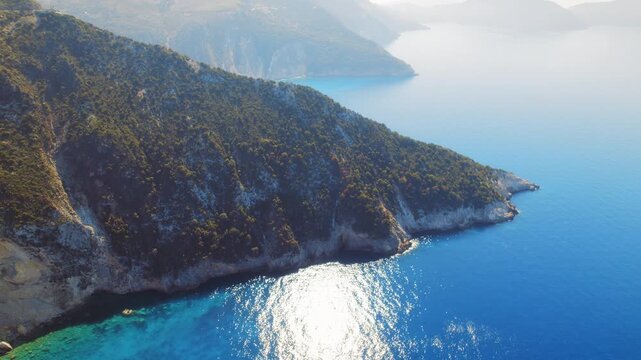 Aerial view of cinematic sunlit green peninsula meeting the Ionian Sea in Greece