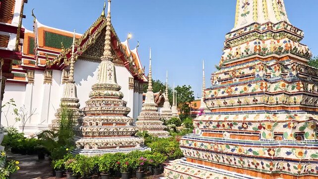 Tourists explore ornate pagodas and temple buildings in Thailand on a sunny day.