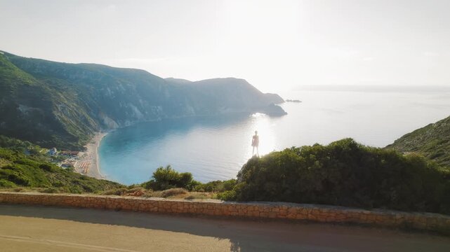 Woman standing on a cliff overlooking a beautiful beach in Kefalonia at sunrise
