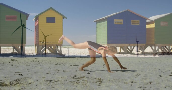 Cartwheeling girl wearing striped one-piece swimsuit on sandy beach, colorful huts on stilts