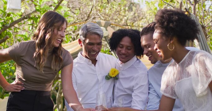 Diverse five adults raising flutes to toast couple, sipping and smiling in garden with yellow rose