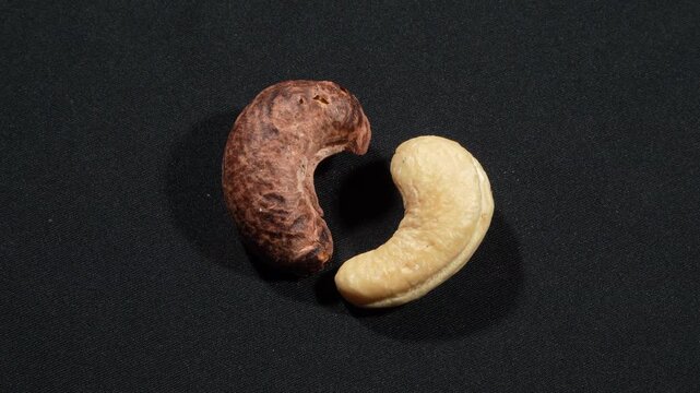 Close-up of two types of cashews forming a symmetrical heart on dark background.