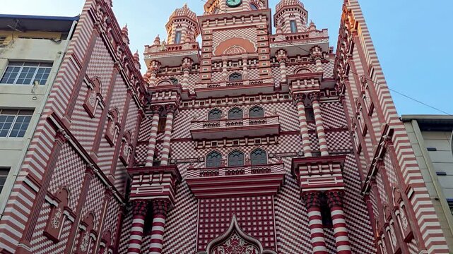 Wide view of Jami Ul-Alfar Mosque (Red Mosque) in Pettah, Colombo, Sri Lanka, showcasing its iconic red and white striped fa&ccedil;ade and distinctive Indo-Islamic architecture in a busy urban setting.