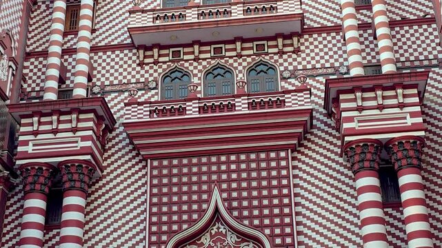 Close-up view of Jami Ul-Alfar Mosque (Red Mosque) in Pettah, Colombo, Sri Lanka, showcasing its iconic red and white striped fa&ccedil;ade and distinctive Indo-Islamic architecture in a busy urban setting.