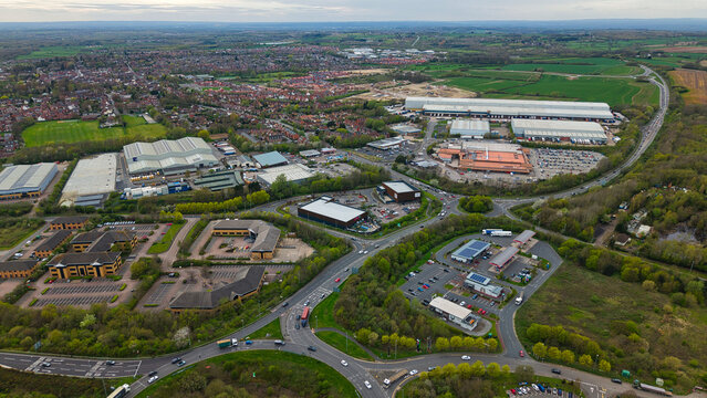 Aerial view of an industrial estate and business park with large warehouses, office buildings, and a busy roundabout in Ashby-de-la-Zouch, England, United Kingdom.