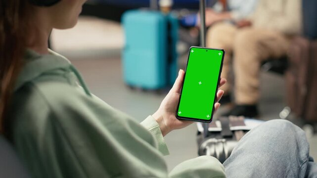 Vertical phone, chroma key screen, digital nomad girl, nomadic lifestyle and global mobility, location independent in airport terminal waiting area. Gen z young woman in the lounge.
