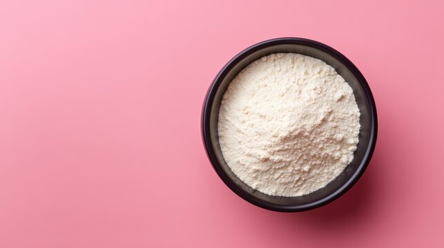 Colostrum milk powder in a black bowl on a smooth pink backdrop