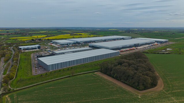 Aerial view of Appleby Magna industrial park featuring large modern warehouses surrounded by green fields and yellow rapeseed crops under an overcast sky in Appleby Magna, England, United Kingdom.