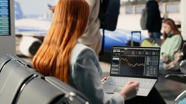 Independent female trader checking financial data and currency exchange, investment performance on laptop in airport waiting area. Busy terminal emphasizes remote trading and nomadic lifestyle.