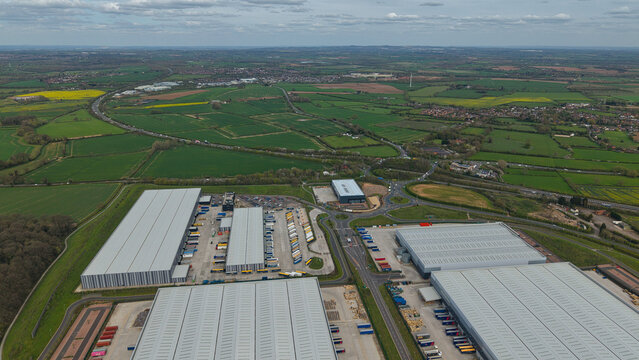 Aerial view of Appleby Magna industrial park with large warehouses, loading docks, and trucks surrounded by green fields in Appleby Magna, England, United Kingdom.