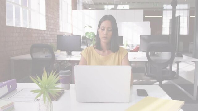 Mature woman pausing typing at laptop in office, resting chin, reflecting while overlays appearing