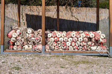 Red and white fishing buoys with rope stacked in outdoor wooden frame, coastal fishing industry equipment, nautical heritage concept. © Masarik
