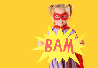 Cute little girl dressed as superhero with paper word BAM on orange background © Pixel-Shot
