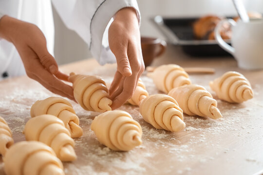 Female baker making croissants at table in kitchen